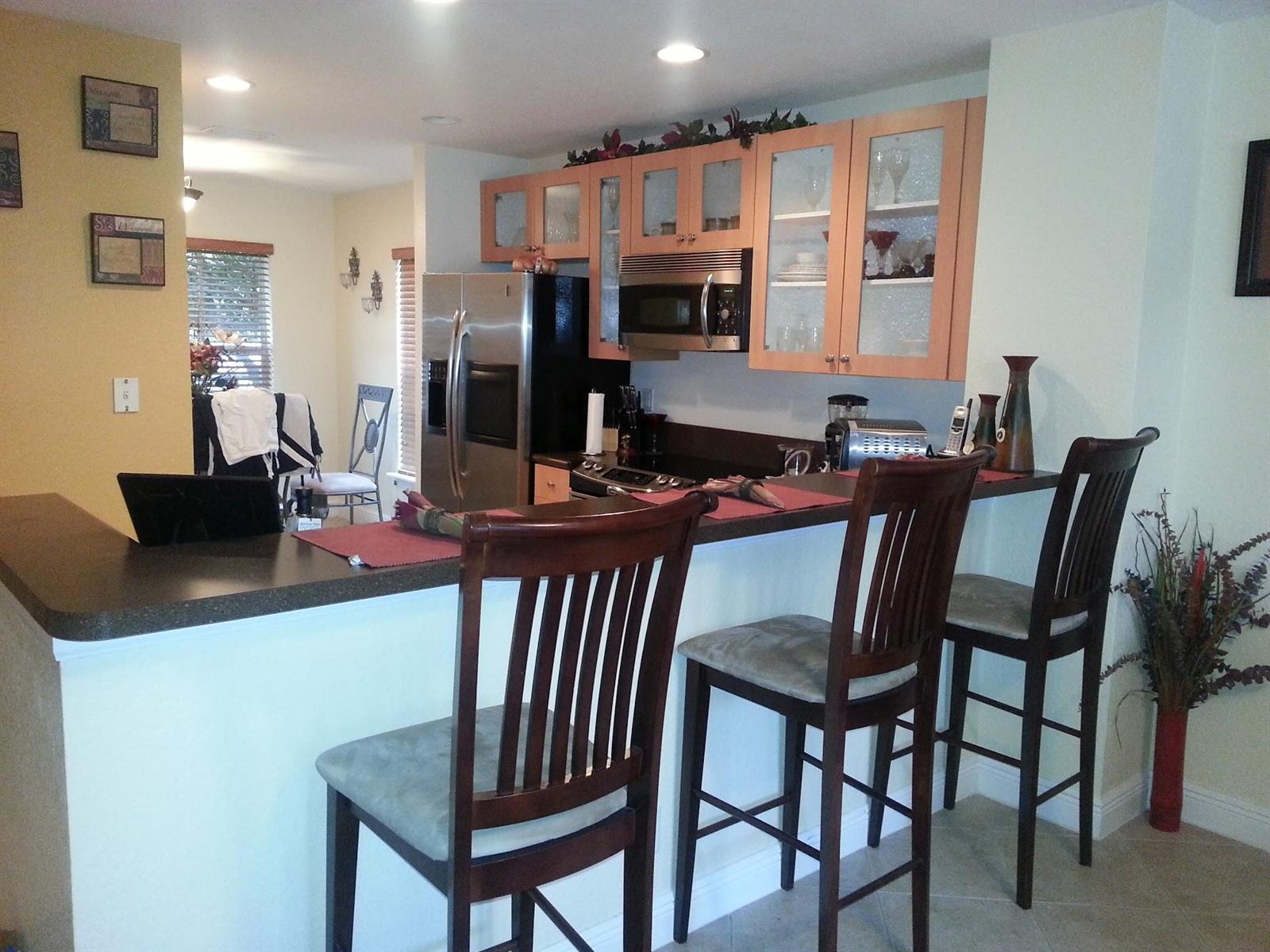 A kitchen features light wood cabinets, stainless steel appliances, and a breakfast bar with stools — 10012 SW 23rd Street, Miramar FL 33025, MIRAMAR, FL