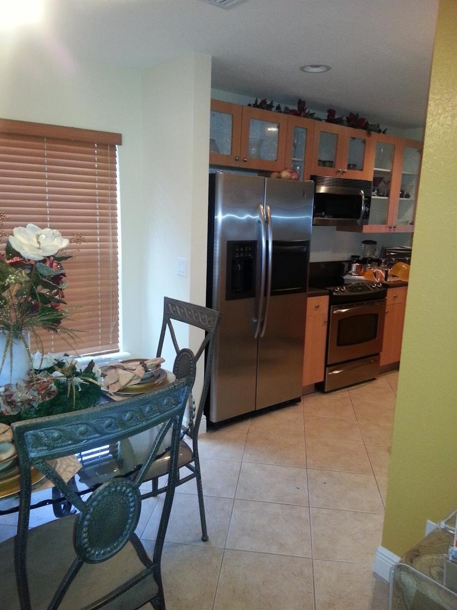 A kitchen with light wood cabinets, stainless steel appliances, and tile flooring next to a dining area — 10012 SW 23rd Street, Miramar FL 33025, MIRAMAR, FL