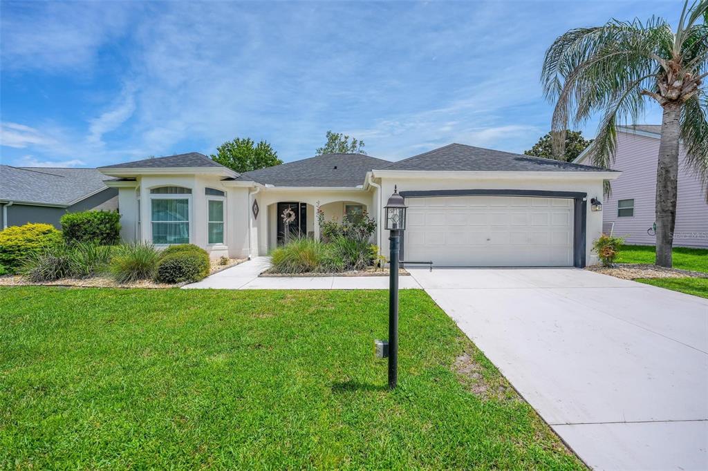 A single-story house with a white exterior, a two-car garage, and a palm tree — 1511 LAVACA LANE, LADY LAKE, FL