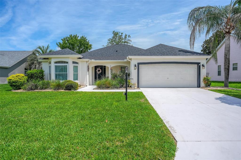 A single-story house with a white exterior, dark roof, and a two-car garage — 1511 LAVACA LANE, LADY LAKE, FL