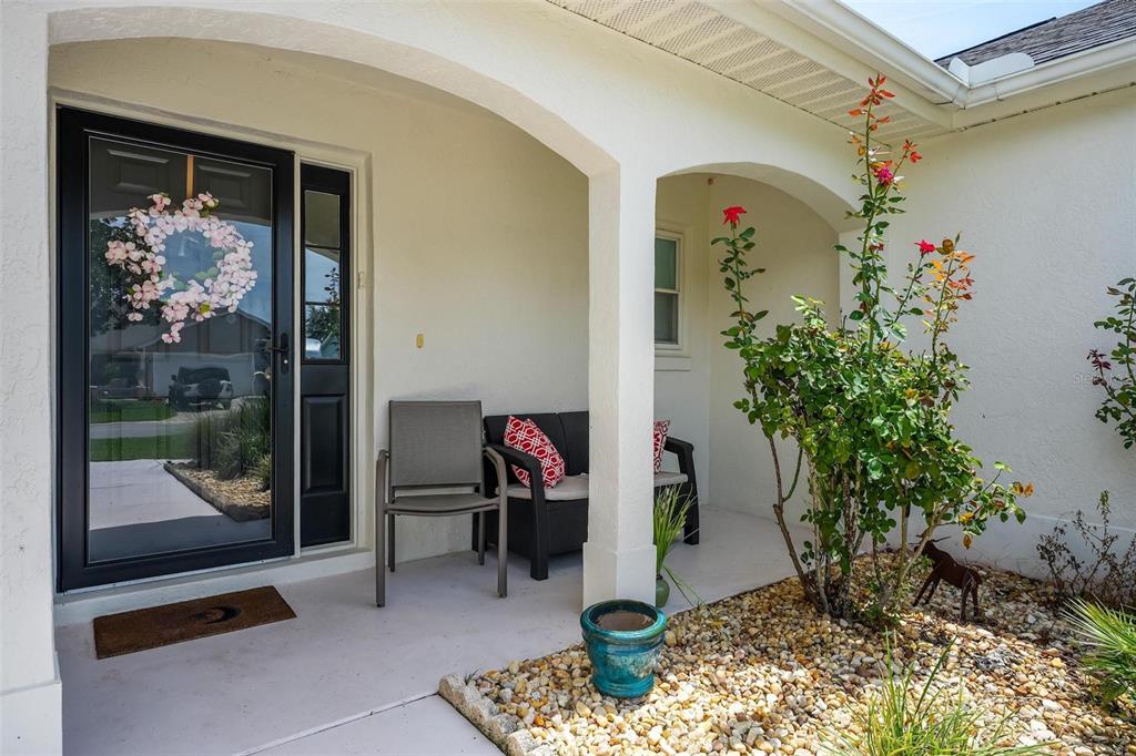 A covered front porch features a black storm door, patio furniture, and a small garden bed — 1511 LAVACA LANE, LADY LAKE, FL