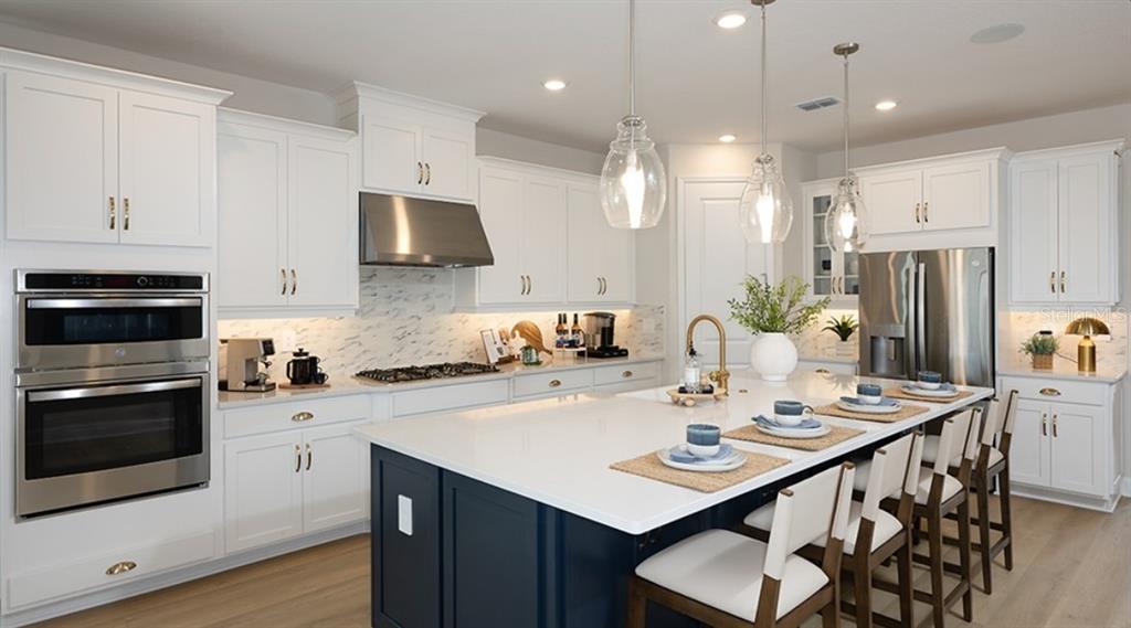 A modern kitchen features white cabinets, a dark blue island, stainless steel appliances, and pendants — 5292 GOLDFINCH DRIVE, ST CLOUD, FL
