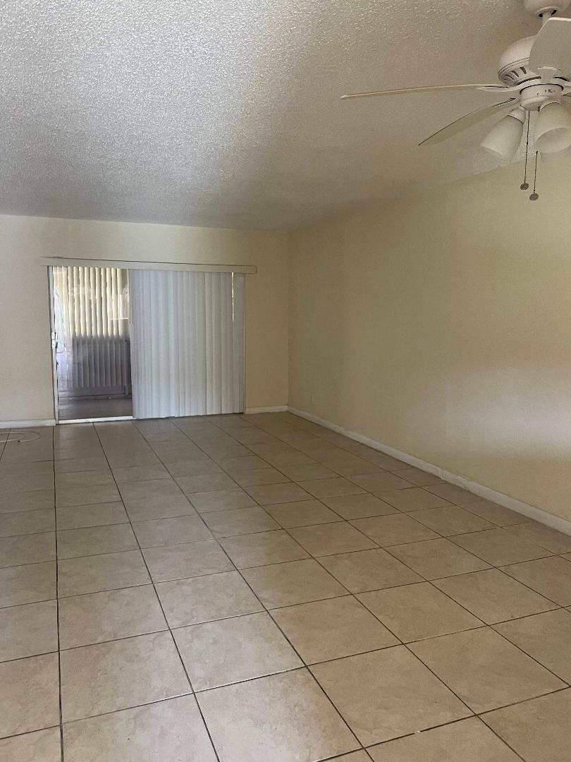 An empty living room features beige tile flooring, light-colored walls, and a ceiling fan — 603 S State Road 7 # 1c, Margate FL 33068, MARGATE, FL