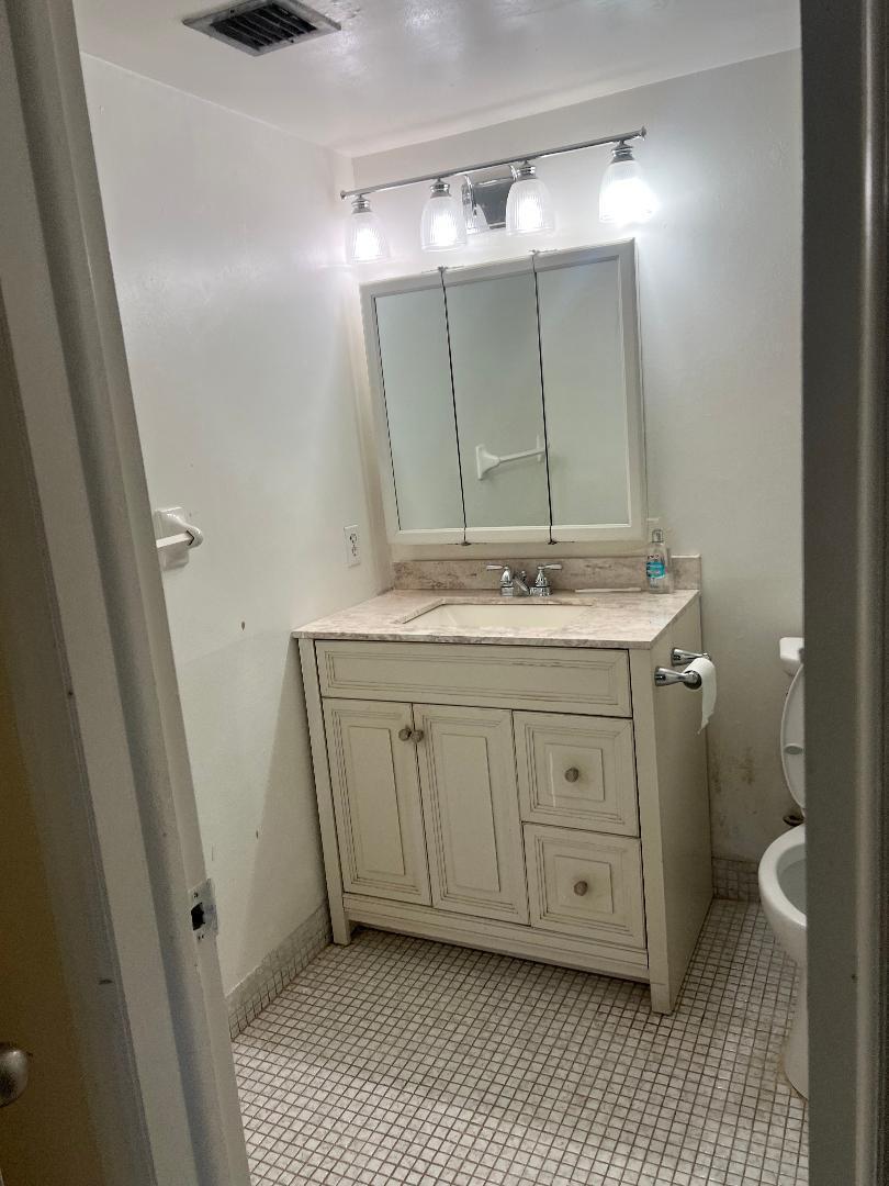A small bathroom features a white vanity with a stone countertop, a medicine cabinet, and tile flooring — 603 S State Road 7 # 1c, Margate FL 33068, MARGATE, FL