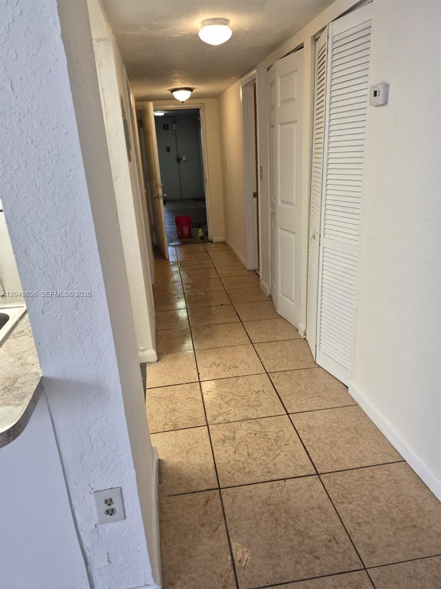 A hallway with beige tile flooring leads to a doorway with a red bucket inside — 16220 NW 2nd Ave # 412, Miami FL 33169, MIAMI, FL