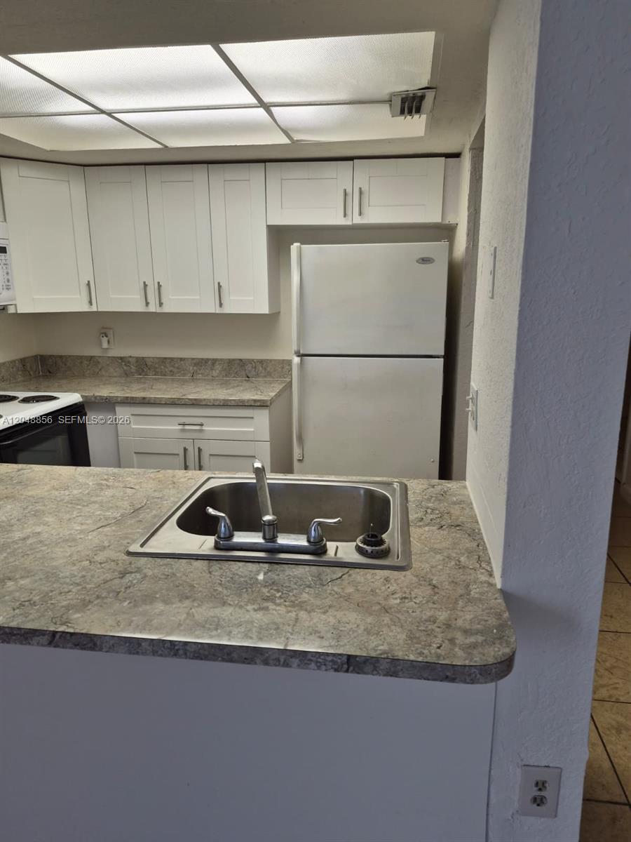 A kitchen features white cabinets, a white refrigerator, and a sink on a peninsula — 16220 NW 2nd Ave # 412, Miami FL 33169, MIAMI, FL