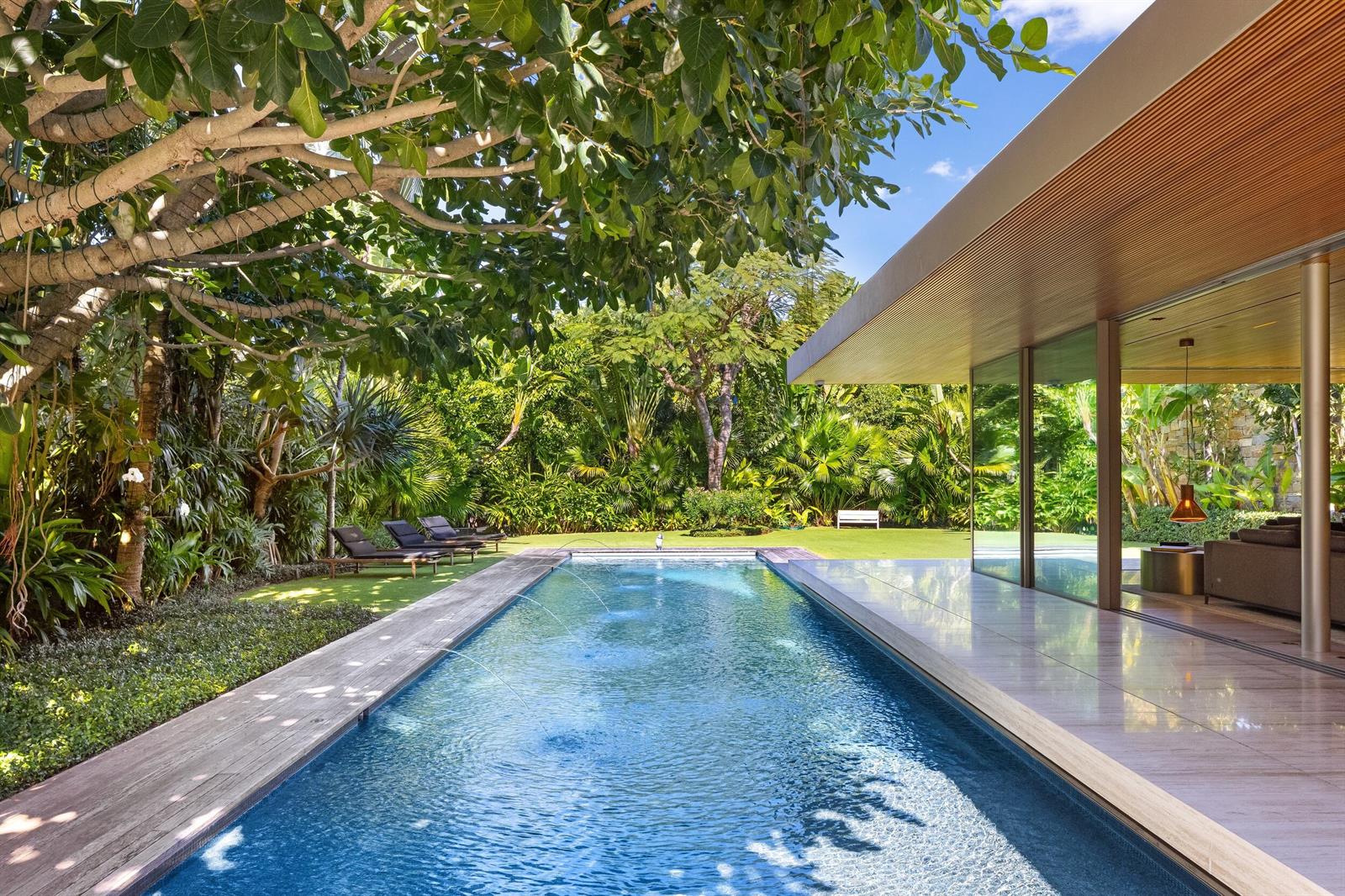 A rectangular swimming pool with fountains sits beside a modern house with a wooden ceiling — 195 Via Marina, Palm Beach FL 33480, PALM BEACH, FL