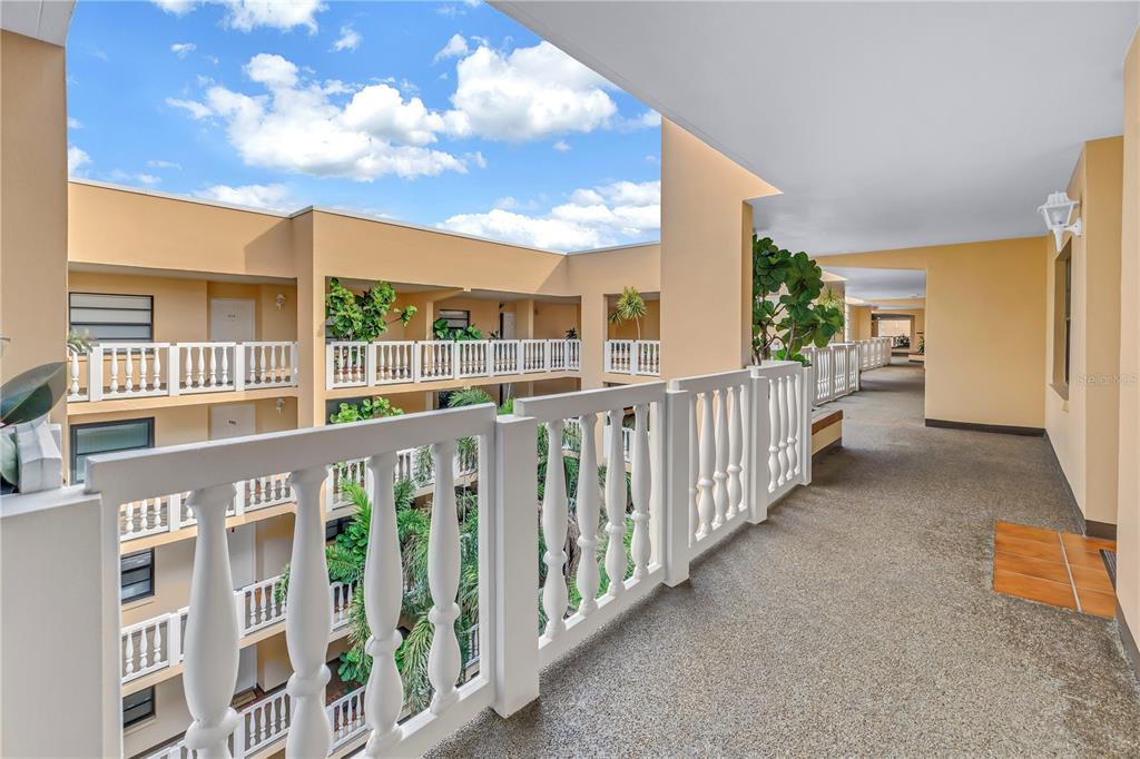 An outdoor balcony walkway overlooks a multi-story apartment complex courtyard with white railings — 6500 SUNSET WAY UNIT 505, ST PETE BEACH, FL