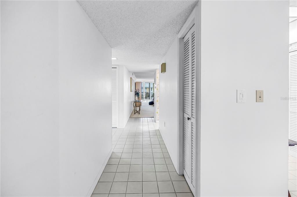 A white hallway with tiled floors leads to a living area with a glass table — 6500 SUNSET WAY UNIT 505, ST PETE BEACH, FL
