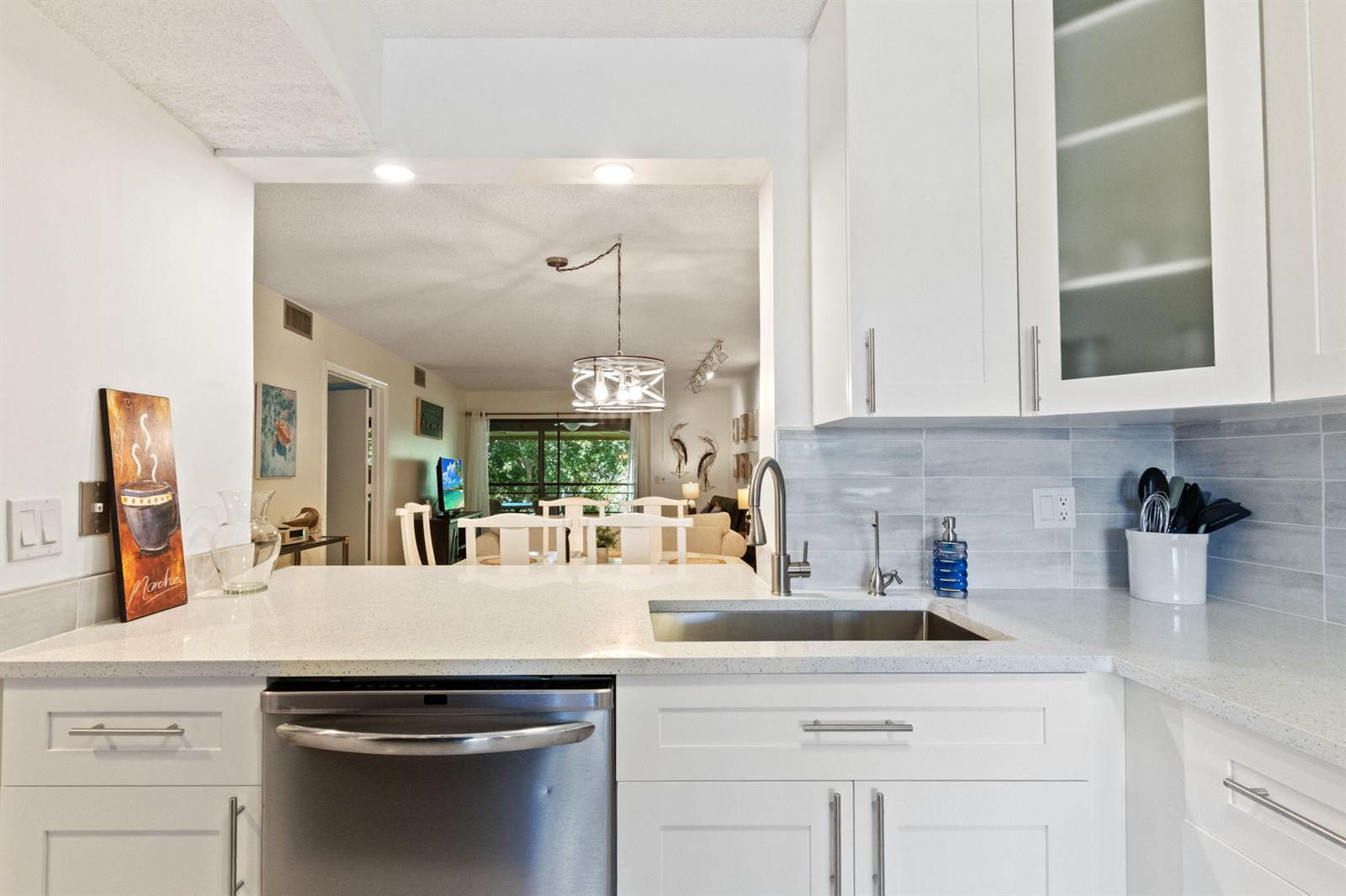 A kitchen with white cabinets, quartz countertops, and a stainless steel dishwasher overlooks a dining area — 5380 Cedar Lake Drive # 304, Boynton Beach FL 33437, BOYNTON BEACH, FL