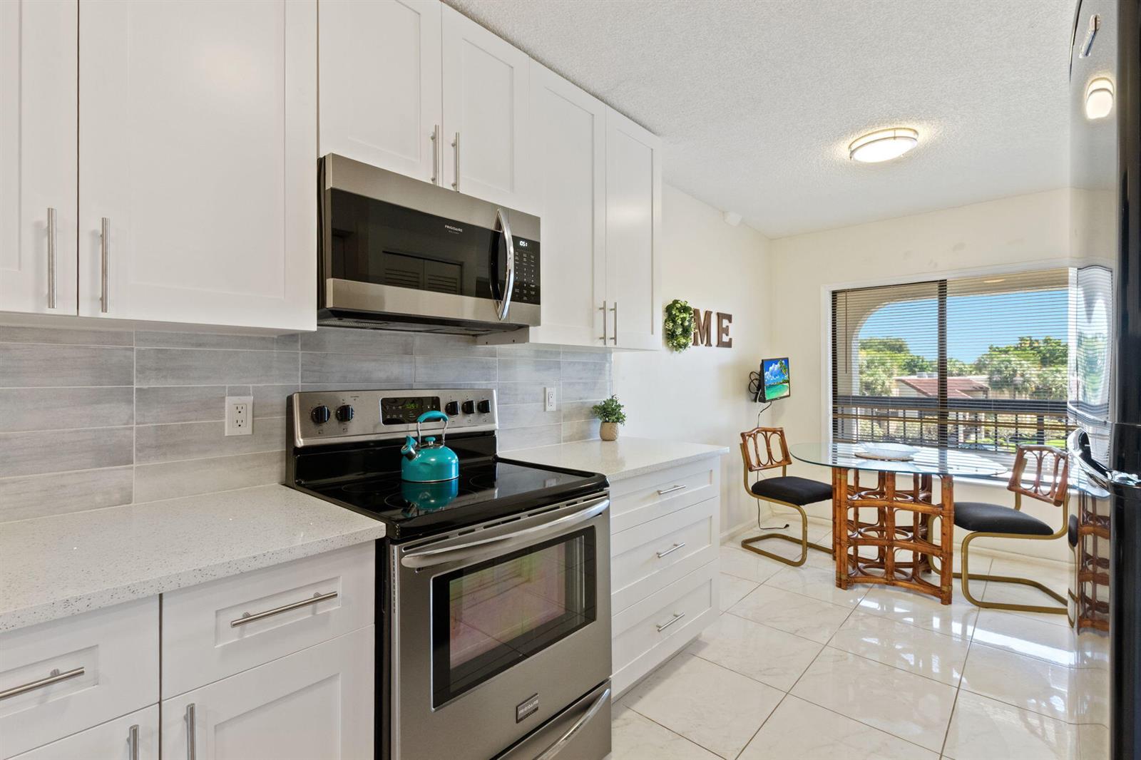 A modern kitchen features white cabinets, stainless steel appliances, and a dining area by windows — 5380 Cedar Lake Drive # 304, Boynton Beach FL 33437, BOYNTON BEACH, FL