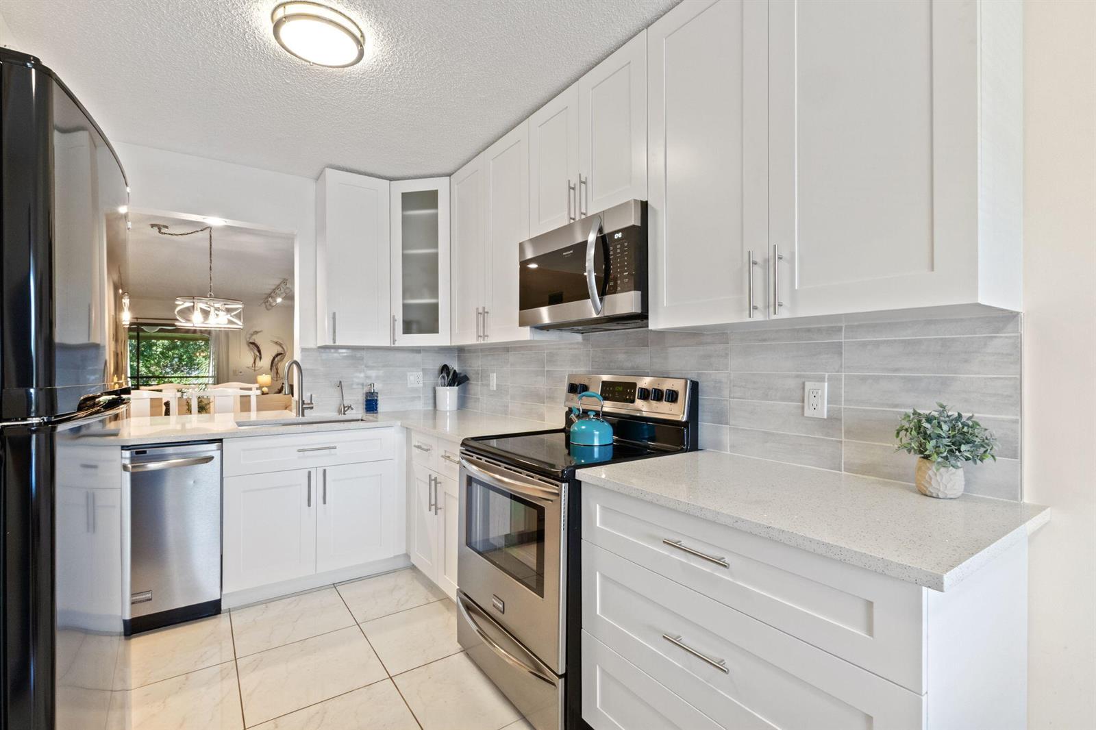 A modern kitchen features white cabinets, stainless steel appliances, quartz countertops, and light tile flooring — 5380 Cedar Lake Drive # 304, Boynton Beach FL 33437, BOYNTON BEACH, FL