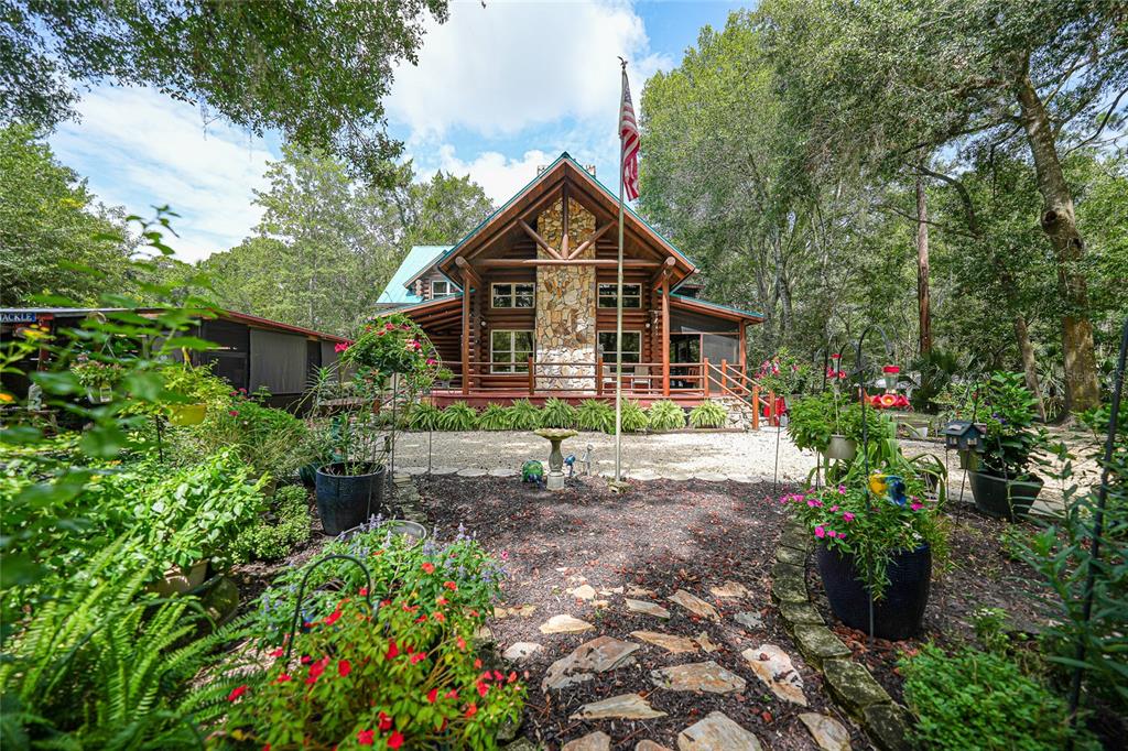 A log cabin home features a stone chimney, a front porch, and a landscaped yard — 8199 W PINOAK COURT, HOMOSASSA, FL