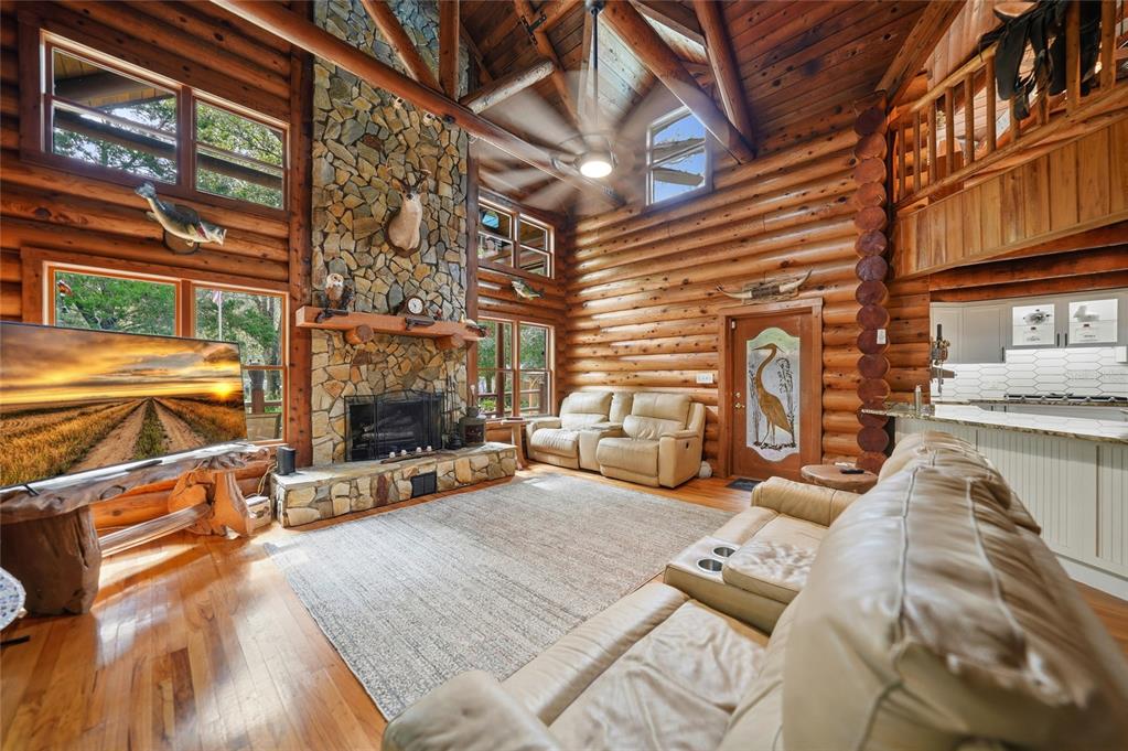 A rustic log cabin living room features a stone fireplace, vaulted ceilings, and leather furniture — 8199 W PINOAK COURT, HOMOSASSA, FL