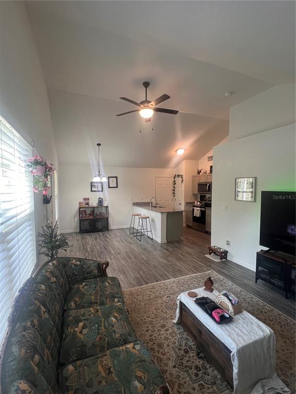 An open-concept living room and kitchen featuring vaulted ceilings, wood-look flooring, and a breakfast bar — 10444 SE 126TH STREET, BELLEVIEW, FL