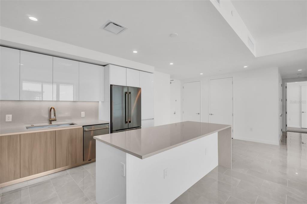 A modern kitchen features white glossy cabinets, wood-tone lower cabinets, a gray island, and stainless appliances — 400 CENTRAL AVENUE UNIT 2605, ST PETERSBURG, FL