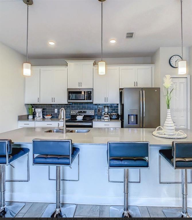 A kitchen features white cabinets, stainless steel appliances, a dark tile backsplash, and a breakfast bar — 452 OCEAN COURSE AVENUE, DAVENPORT, FL