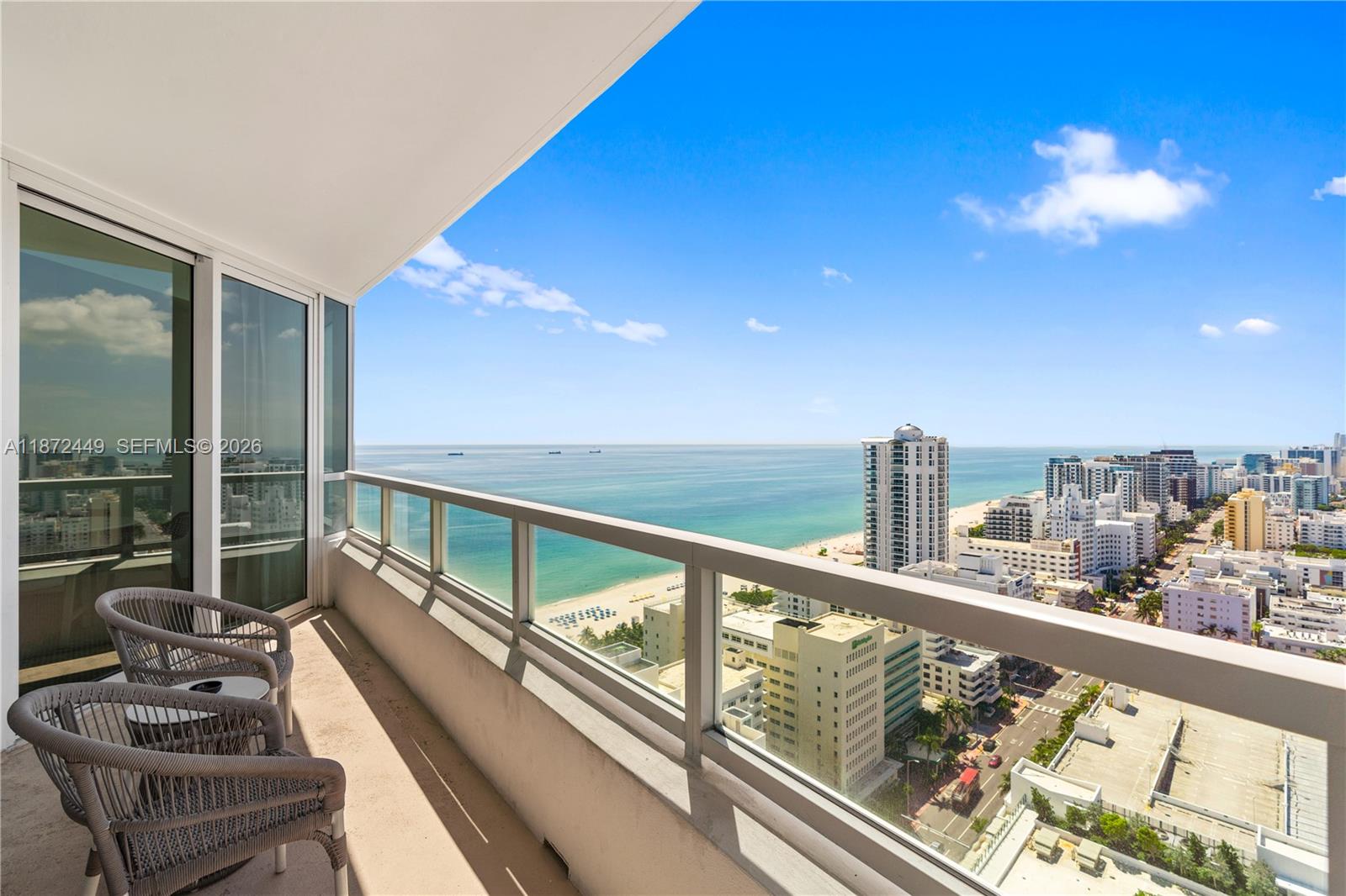 A balcony with two chairs overlooks a beach, ocean, and city skyline — 4401 Collins Ave # 2712, Miami Beach FL 33140, MIAMI BEACH, FL