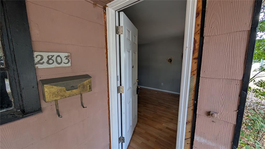 An open white door reveals a room with wood-look flooring and a damaged wall — 2801 W CLEVELAND STREET, TAMPA, FL