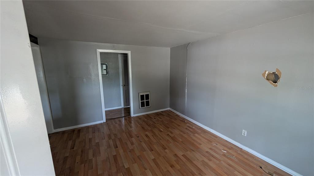 An empty room features gray walls, wood-look flooring, and a hole in the drywall — 2801 W CLEVELAND STREET, TAMPA, FL