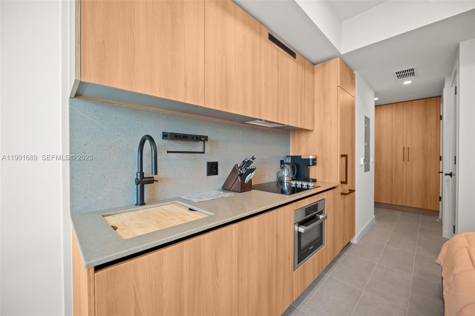 A modern kitchenette features light wood cabinetry, a grey stone countertop, and a black faucet — 121 NE 5 ST # 3507, Miami FL 33132, MIAMI, FL