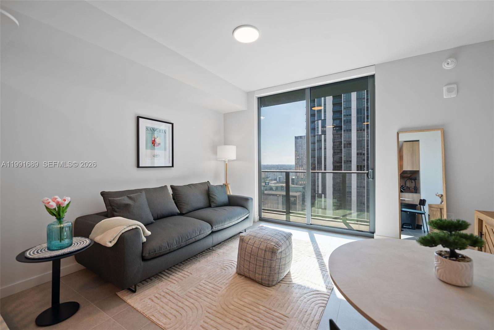 A living room features a grey sofa, a patterned ottoman, and a balcony with city views — 121 NE 5 ST # 3507, Miami FL 33132, MIAMI, FL
