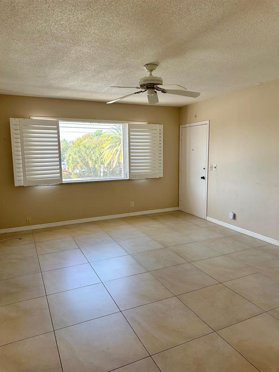An empty room features beige tile flooring, a ceiling fan, and white plantation window shutters — 350 S Cypress Road # 522, Pompano Beach FL 33060, POMPANO BEACH, FL