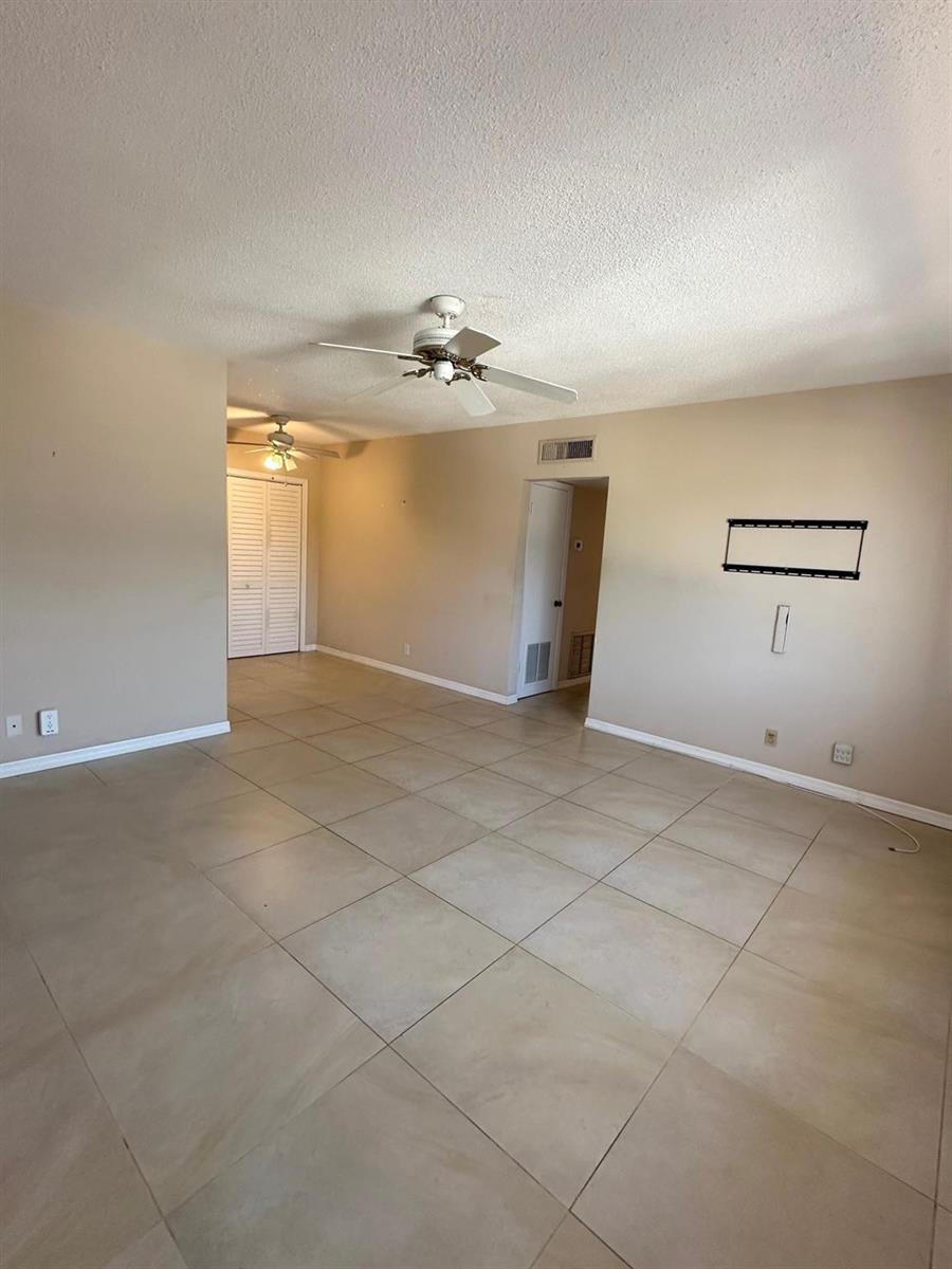 An empty living room features beige tile flooring, tan walls, and two ceiling fans — 350 S Cypress Road # 522, Pompano Beach FL 33060, POMPANO BEACH, FL
