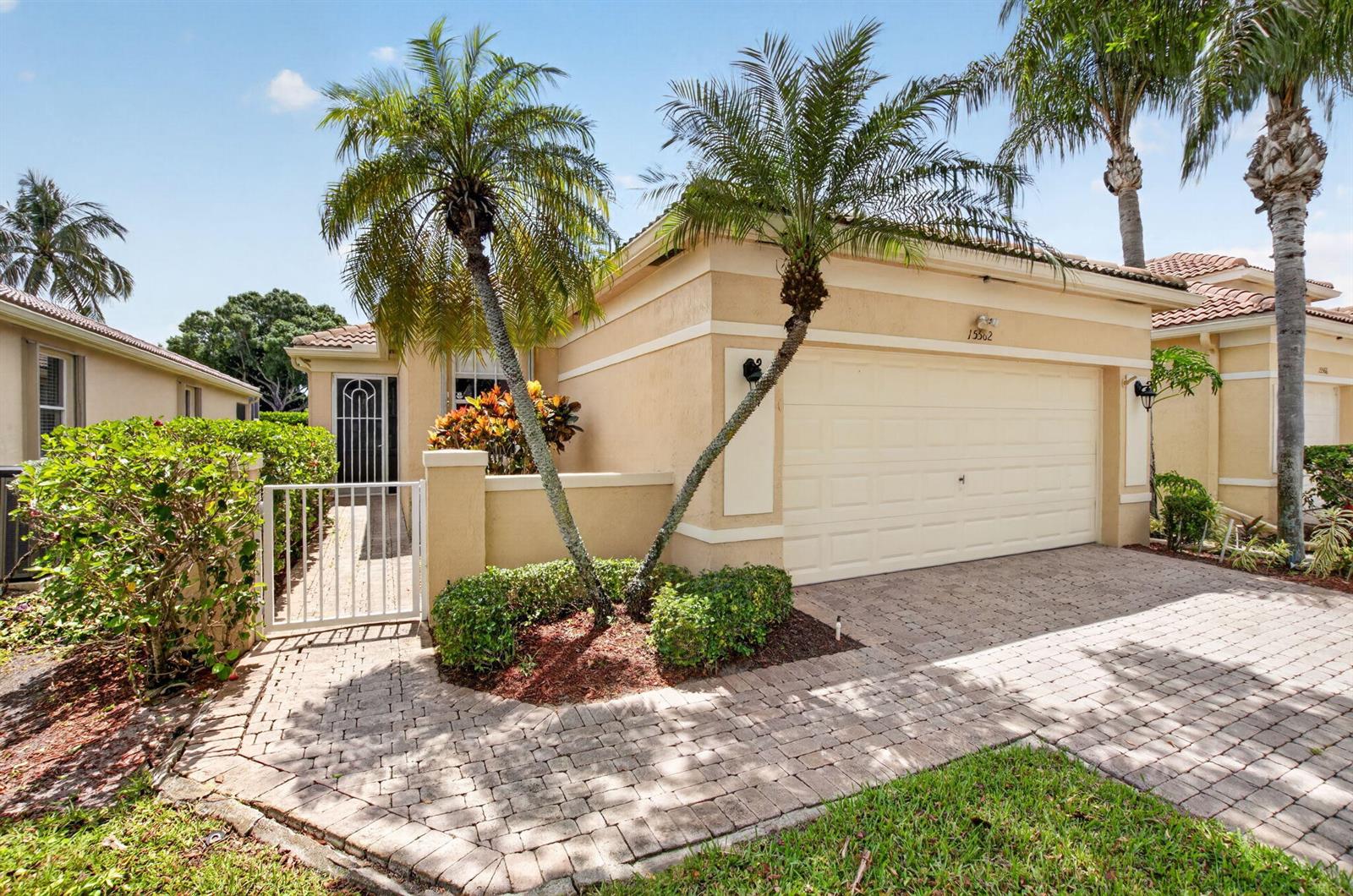 A beige single-story house features a paved driveway, a two-car garage, and two palm trees — 15562 Fiorenza Circle, Delray Beach FL 33446, DELRAY BEACH, FL