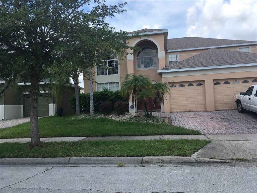 A two-story suburban house with a tan stucco exterior and a three-car garage — 5948 WINCHESTER ISLE ROAD, ORLANDO, FL