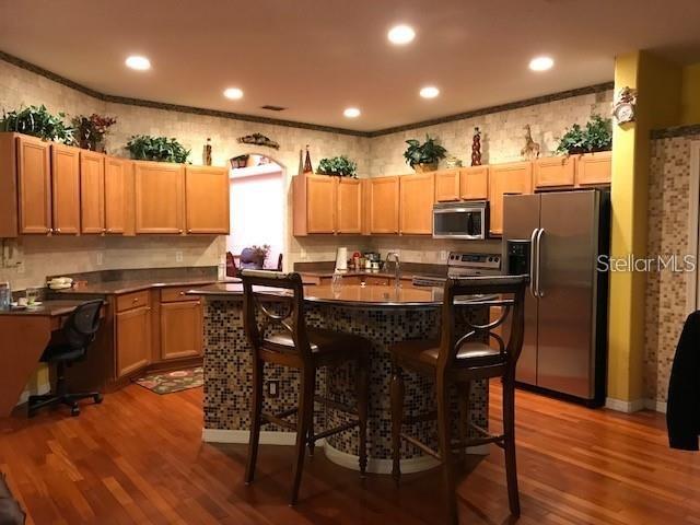 A kitchen features wood cabinets, a tiled island with bar stools, and stainless steel appliances — 5948 WINCHESTER ISLE ROAD, ORLANDO, FL