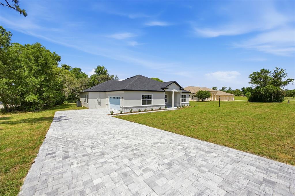 A single-story house with a paved driveway and a large grassy yard under a blue sky — 464 N CHERRY POP DRIVE, INVERNESS, FL