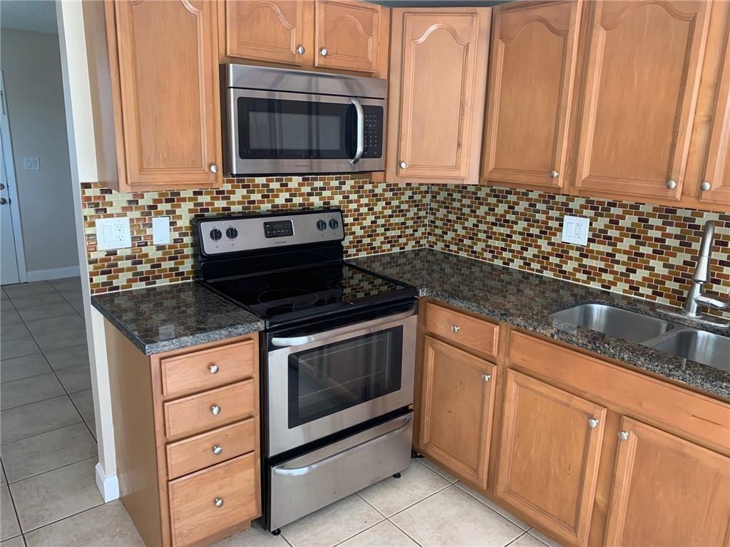 A kitchen features wood cabinets, stainless steel appliances, granite countertops, and a mosaic tile backsplash — 206 SW 1st Street # 4, Pompano Beach FL 33060, POMPANO BEACH, FL