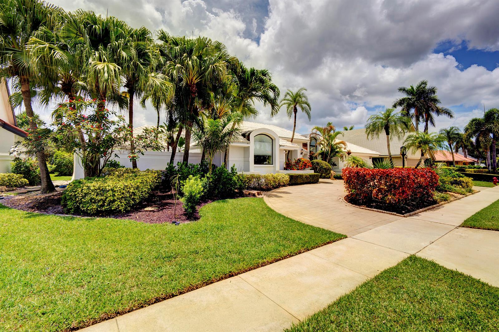 A single-story house with a paved driveway, palm trees, and landscaping under a cloudy sky — 10252 Shireoaks Lane, Boca Raton FL 33498, BOCA RATON, FL
