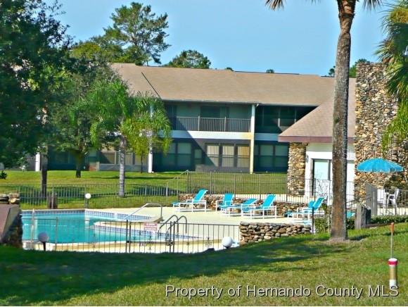A swimming pool sits in front of a multi-story apartment building with a stone chimney — 6460 RIVER RUN BOULEVARD, WEEKI WACHEE, FL