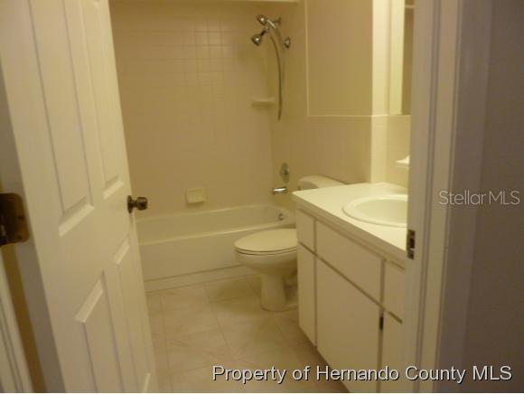 A bathroom features a white vanity, a toilet, and a shower-tub combination with white tile — 6460 RIVER RUN BOULEVARD, WEEKI WACHEE, FL