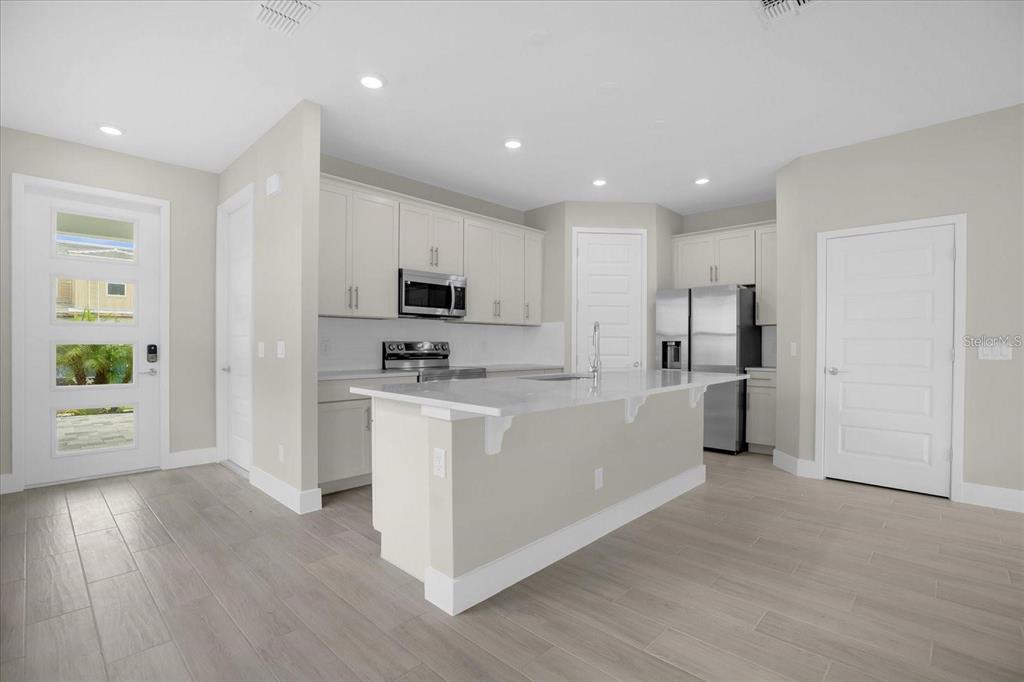 A modern kitchen features white cabinets, a central island, stainless steel appliances, and tile flooring — 7818 SPECTRUM DRIVE, KISSIMMEE, FL