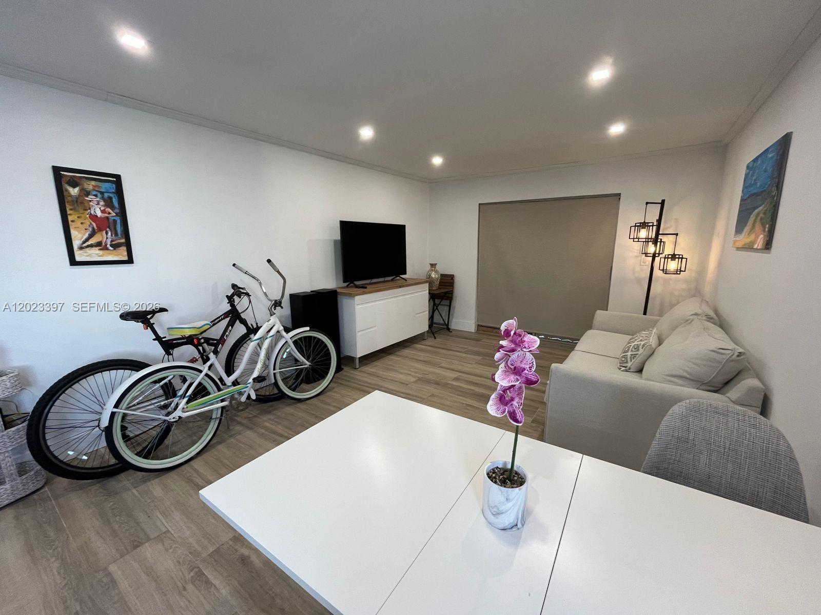 A living room features a white media console, a sofa, and two bicycles parked indoors — 6965 Harding Ave # 401, Miami Beach FL 33141, MIAMI BEACH, FL