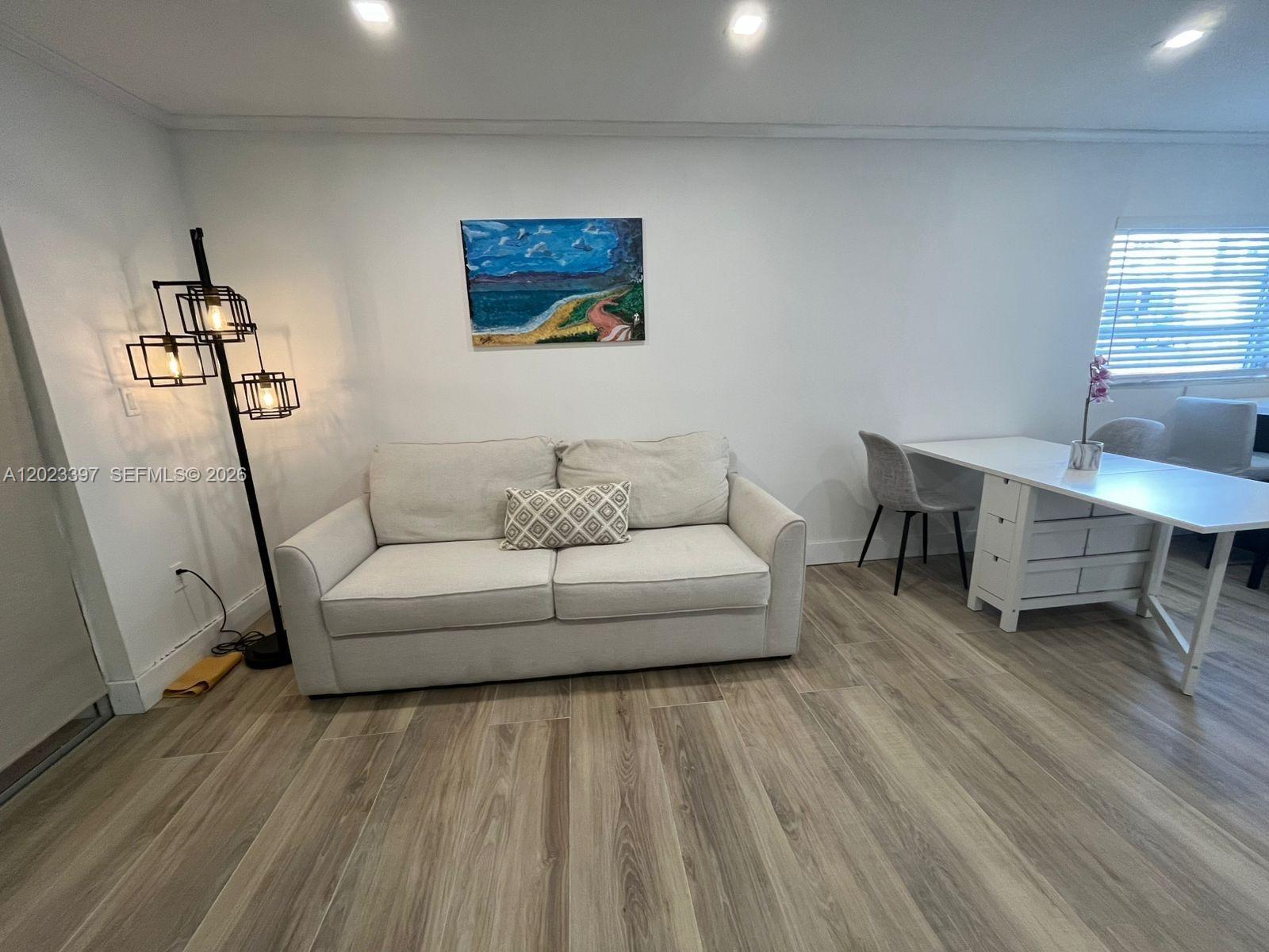 A living room features a light-colored sofa, a floor lamp, and a white desk — 6965 Harding Ave # 401, Miami Beach FL 33141, MIAMI BEACH, FL