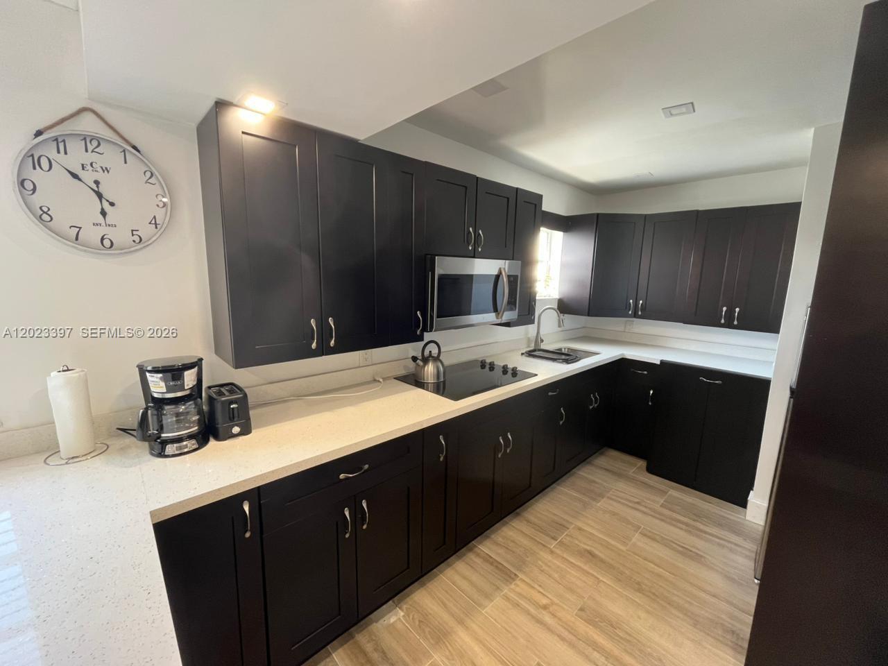 A kitchen features dark cabinets, white countertops, stainless steel appliances, and light wood-look flooring — 6965 Harding Ave # 401, Miami Beach FL 33141, MIAMI BEACH, FL