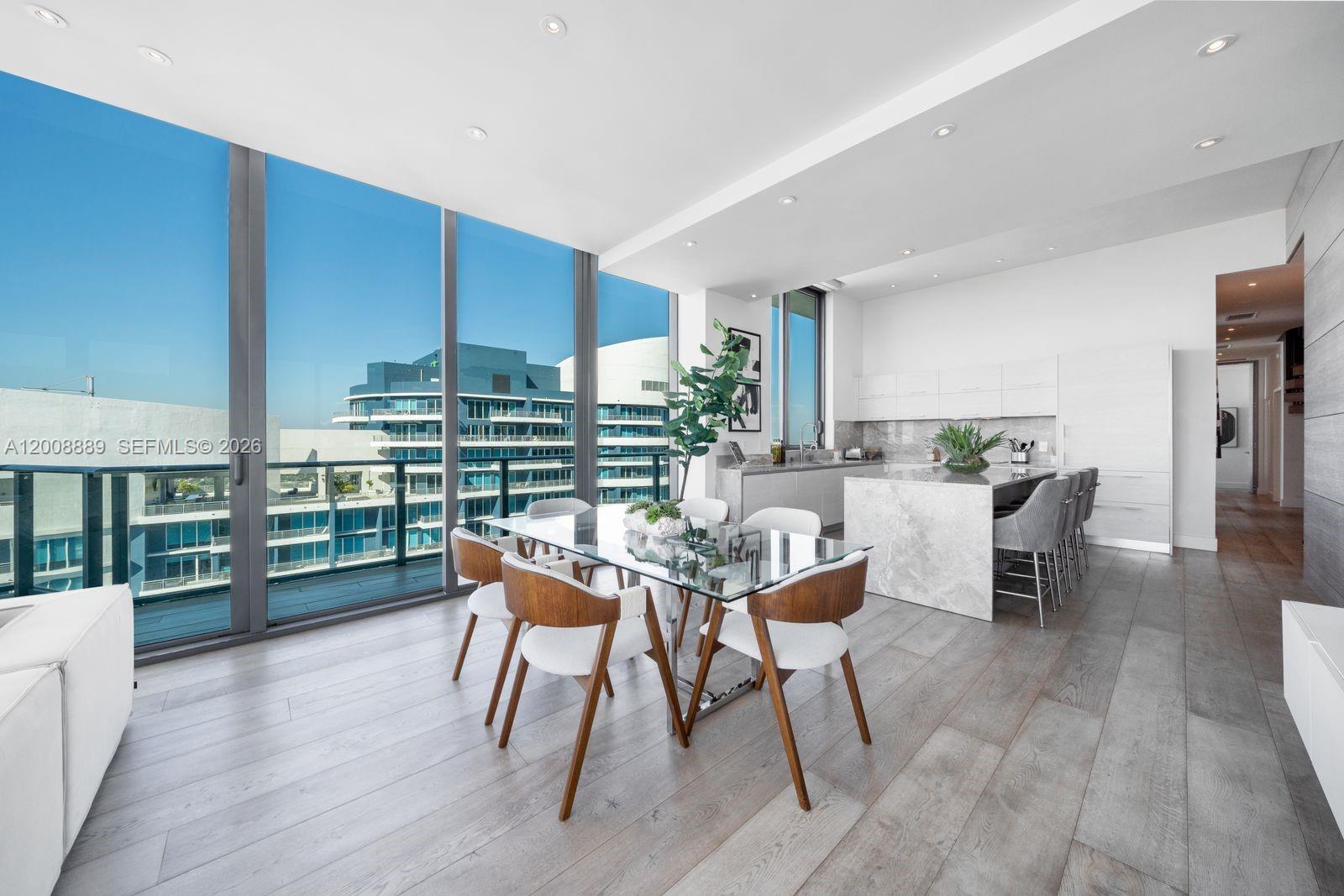 A modern dining area features a glass table, wooden chairs, and floor-to-ceiling windows — 1300 S Miami Ave, Miami FL 33130, MIAMI, FL