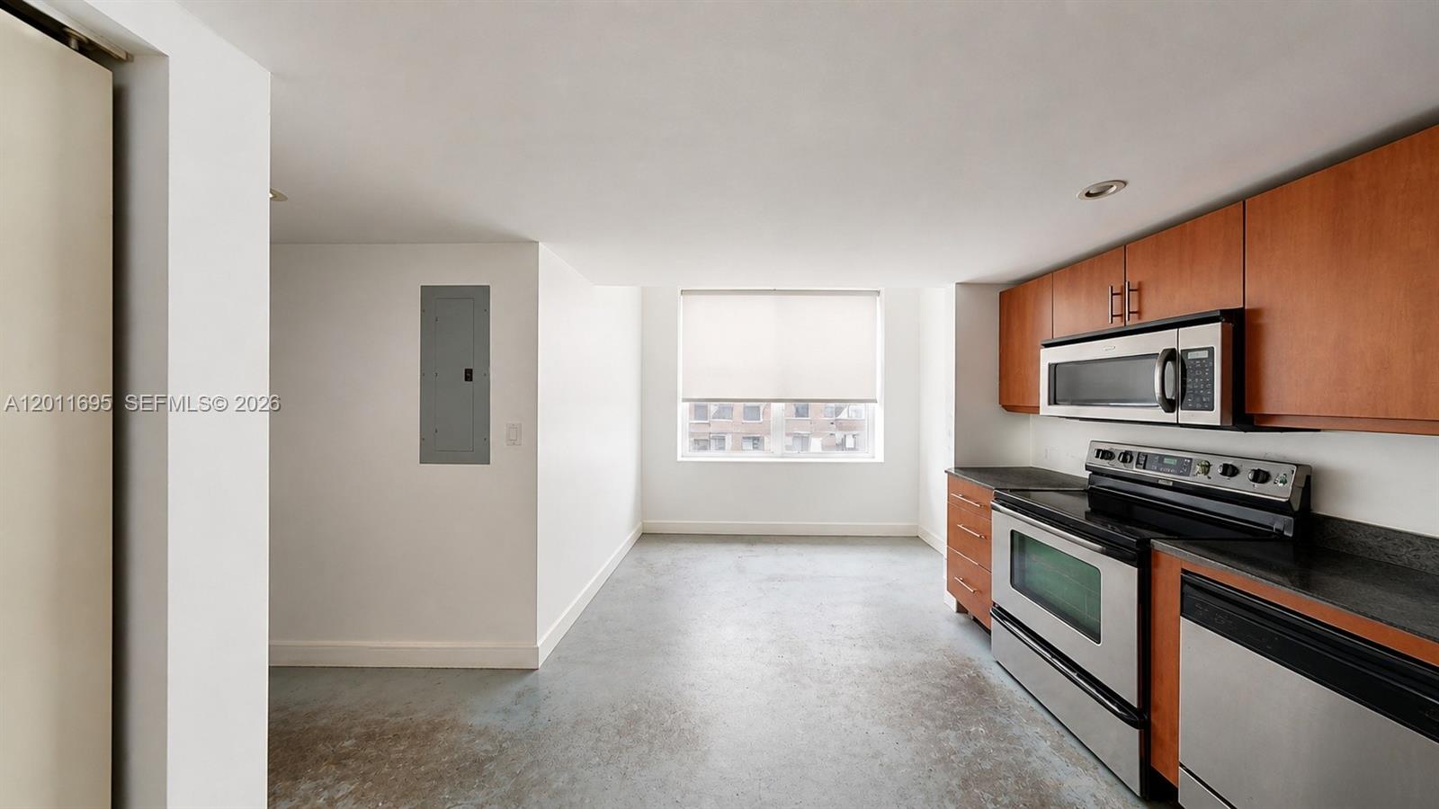 A kitchen with wood cabinets, stainless steel appliances, and concrete flooring faces a window — 111 E Flagler St # 705, Miami FL 33131, MIAMI, FL