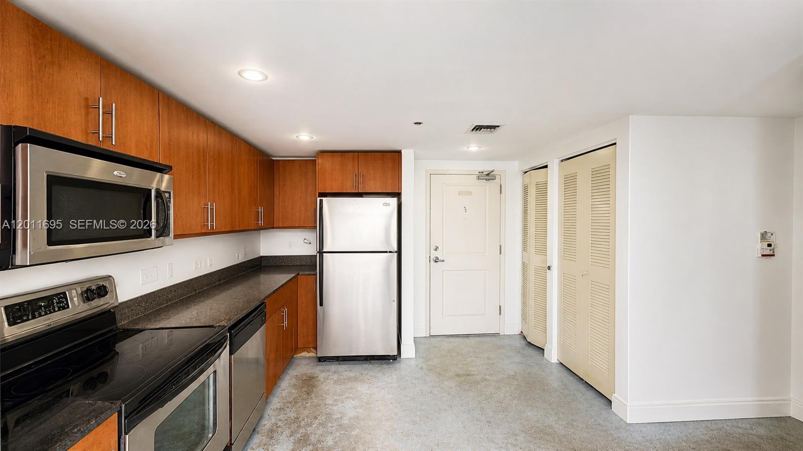 A kitchen features wood cabinets, stainless steel appliances, dark countertops, and a light-colored floor — 111 E Flagler St # 705, Miami FL 33131, MIAMI, FL