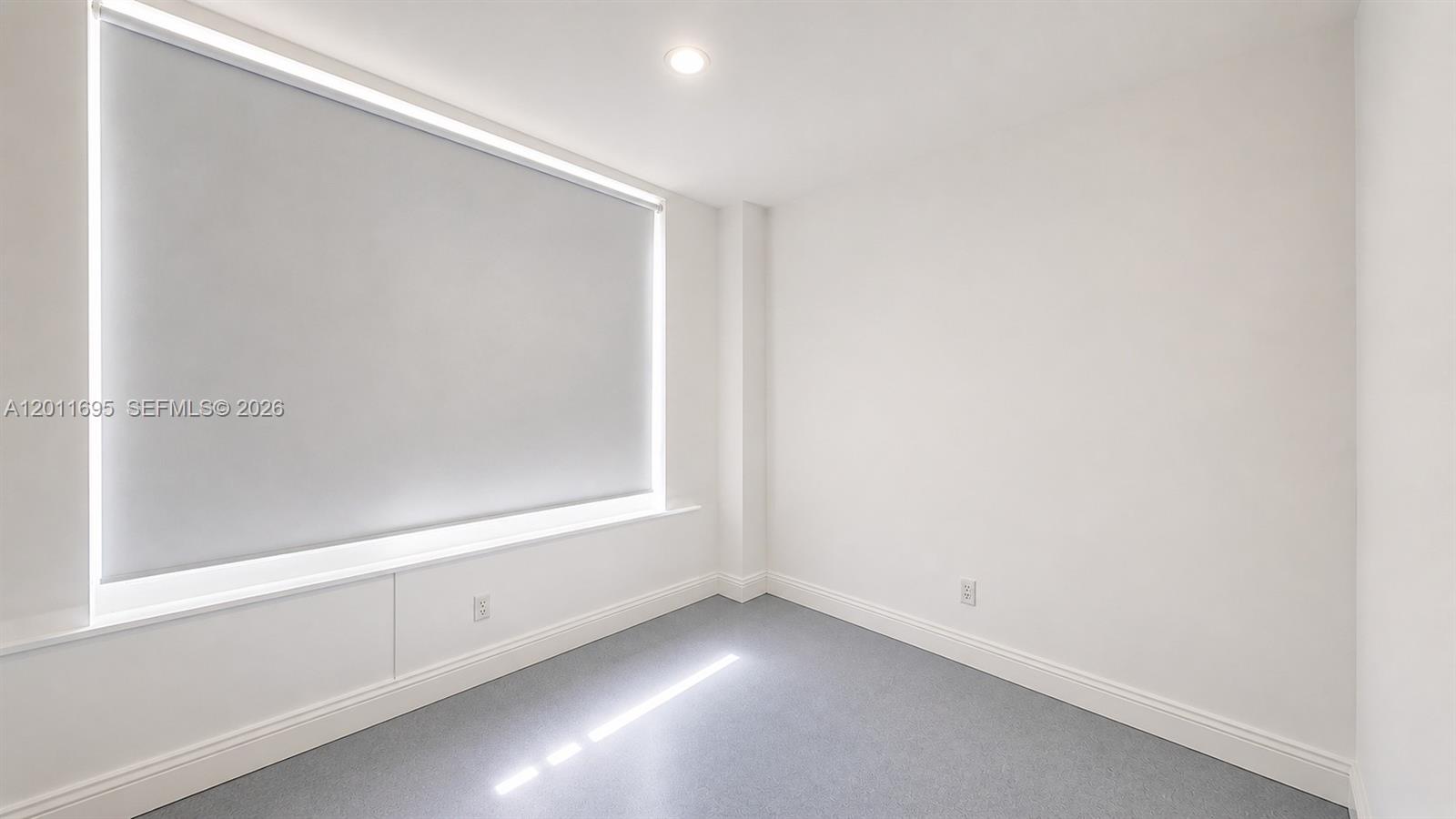 A small, empty room with white walls, a large window with a shade, and gray flooring — 111 E Flagler St # 705, Miami FL 33131, MIAMI, FL