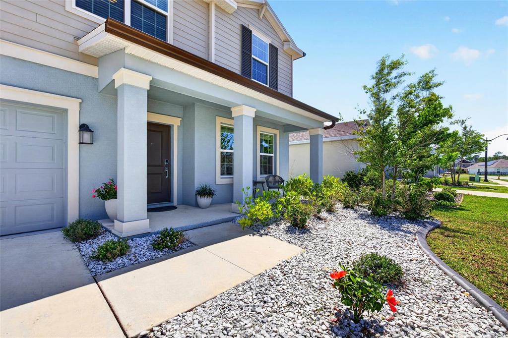The exterior of a light blue house features a covered porch, white columns, and a gravel yard — 223 WINGED FOOT LANE, DAYTONA BEACH, FL