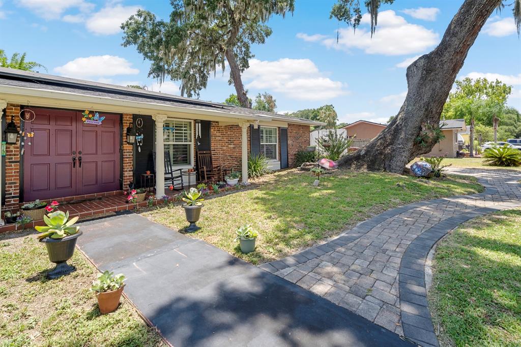 A brick house exterior features a double front door, a paved walkway, and large trees — 802 HASTINGS DRIVE, KISSIMMEE, FL