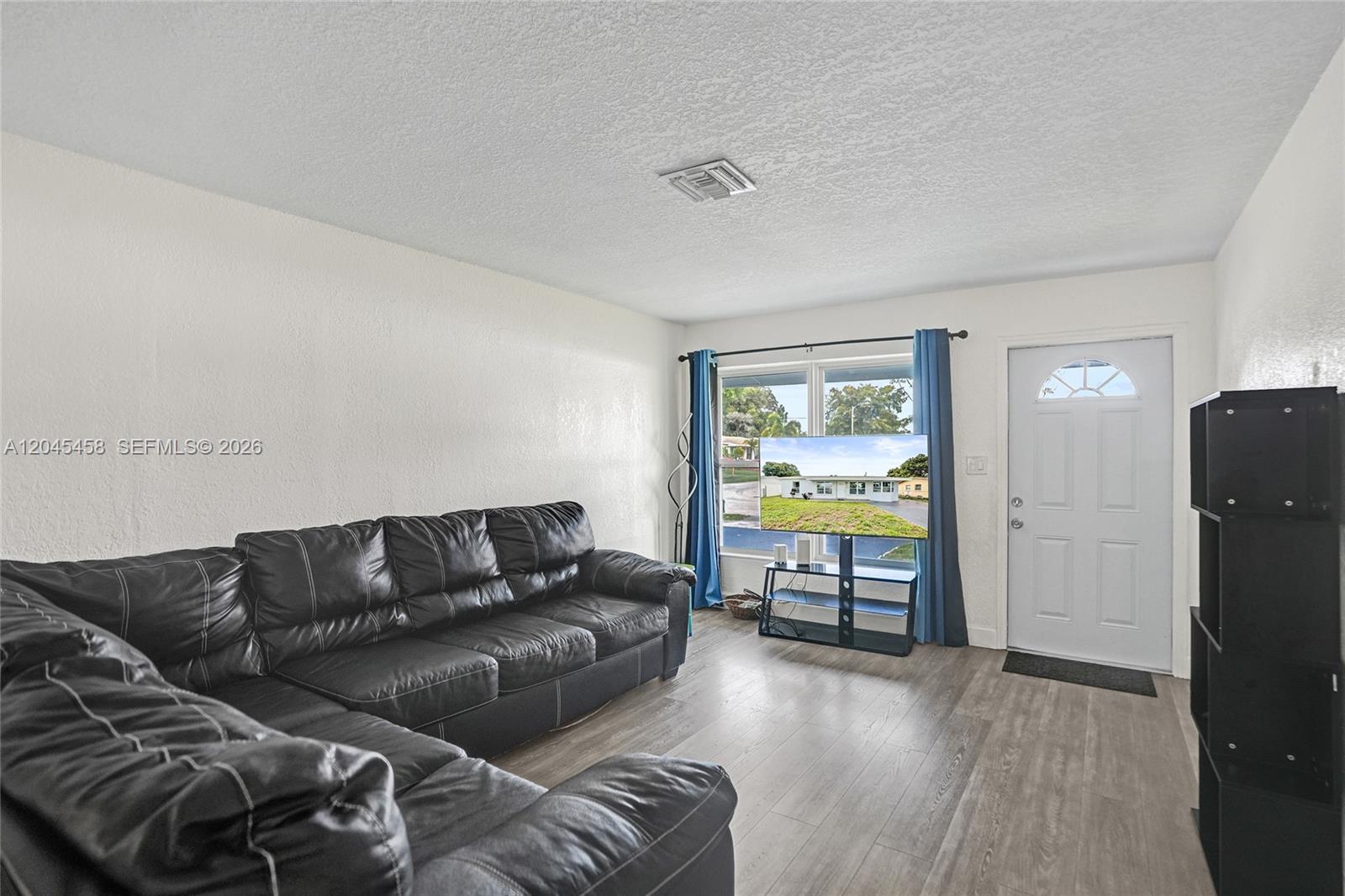 A living room features a black leather sectional, wood-look flooring, and a television near windows — 3320 NW 18th St, Lauderhill FL 33311, LAUDERHILL, FL