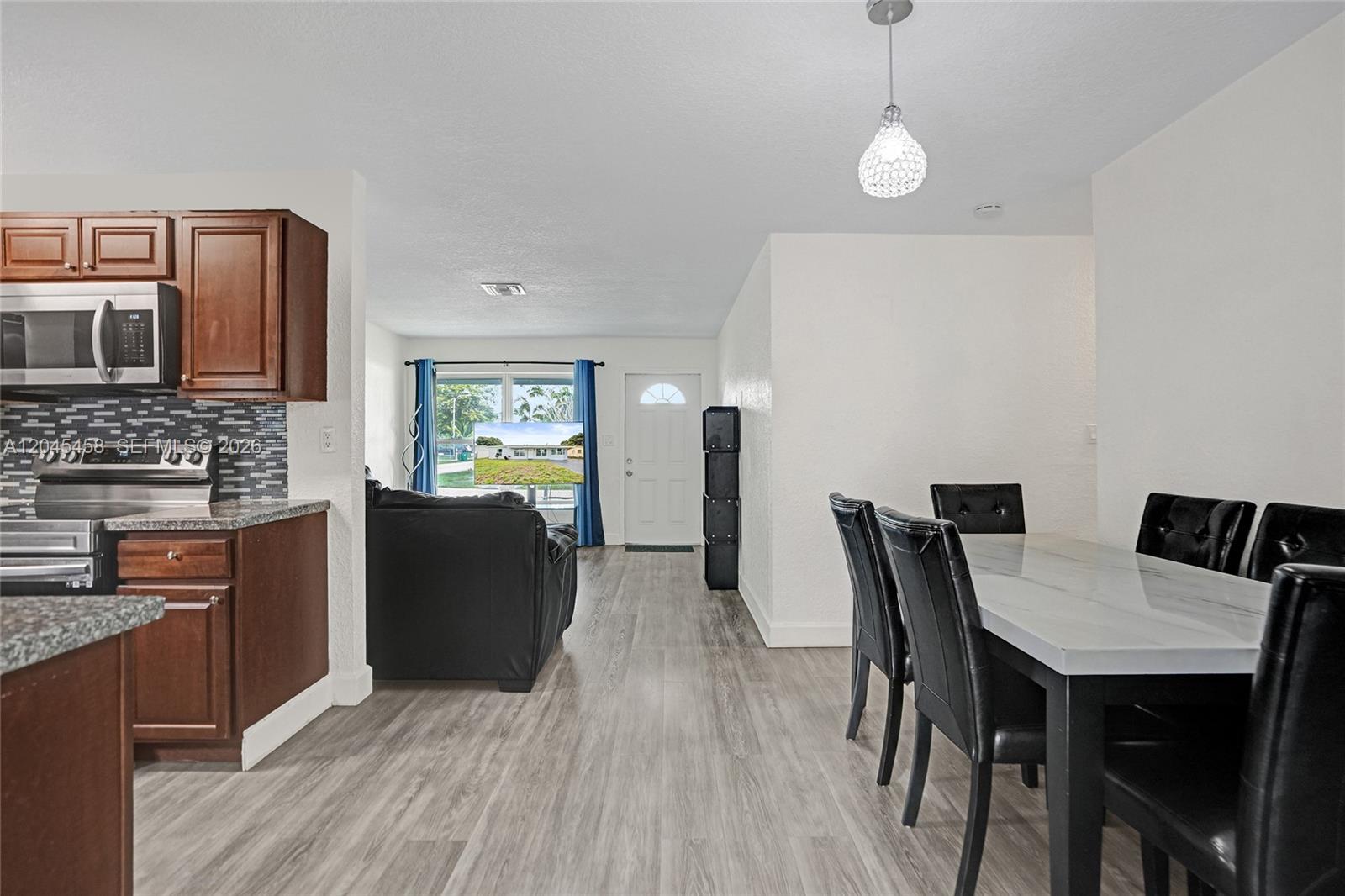 This open-concept kitchen and dining area features wood cabinets, stainless appliances, and light flooring — 3320 NW 18th St, Lauderhill FL 33311, LAUDERHILL, FL