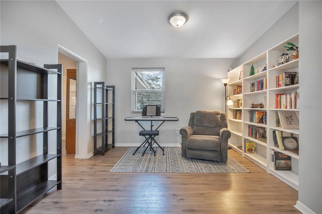 A room with wood-look flooring, built-in white bookshelves, a gray recliner, and a keyboard stand — 5450 ROSE AVENUE, ORLANDO, FL