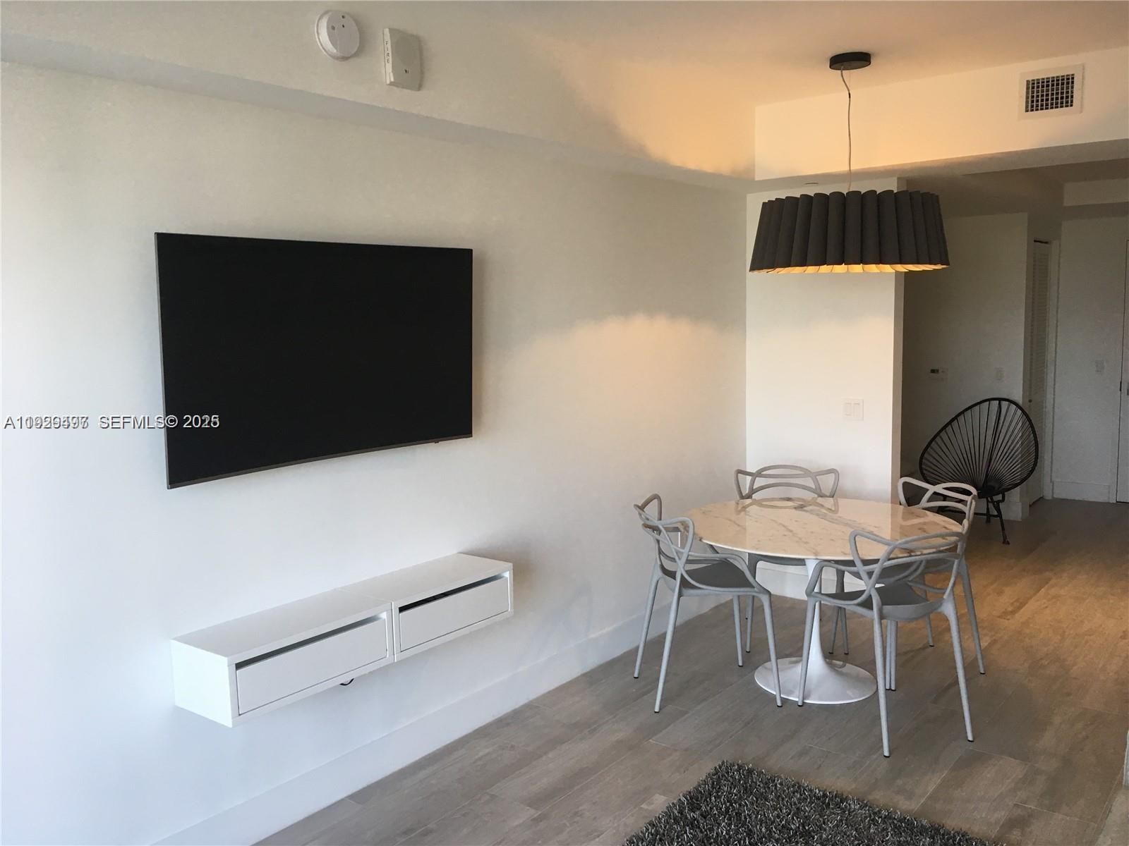 A dining area with a round marble table and chairs sits beside a wall-mounted television — 121 NE 34th St # 1203, Miami FL 33137, MIAMI, FL